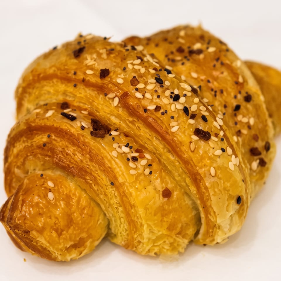 Golden flaky croissant topped with white and black sesame seeds on a white plate.