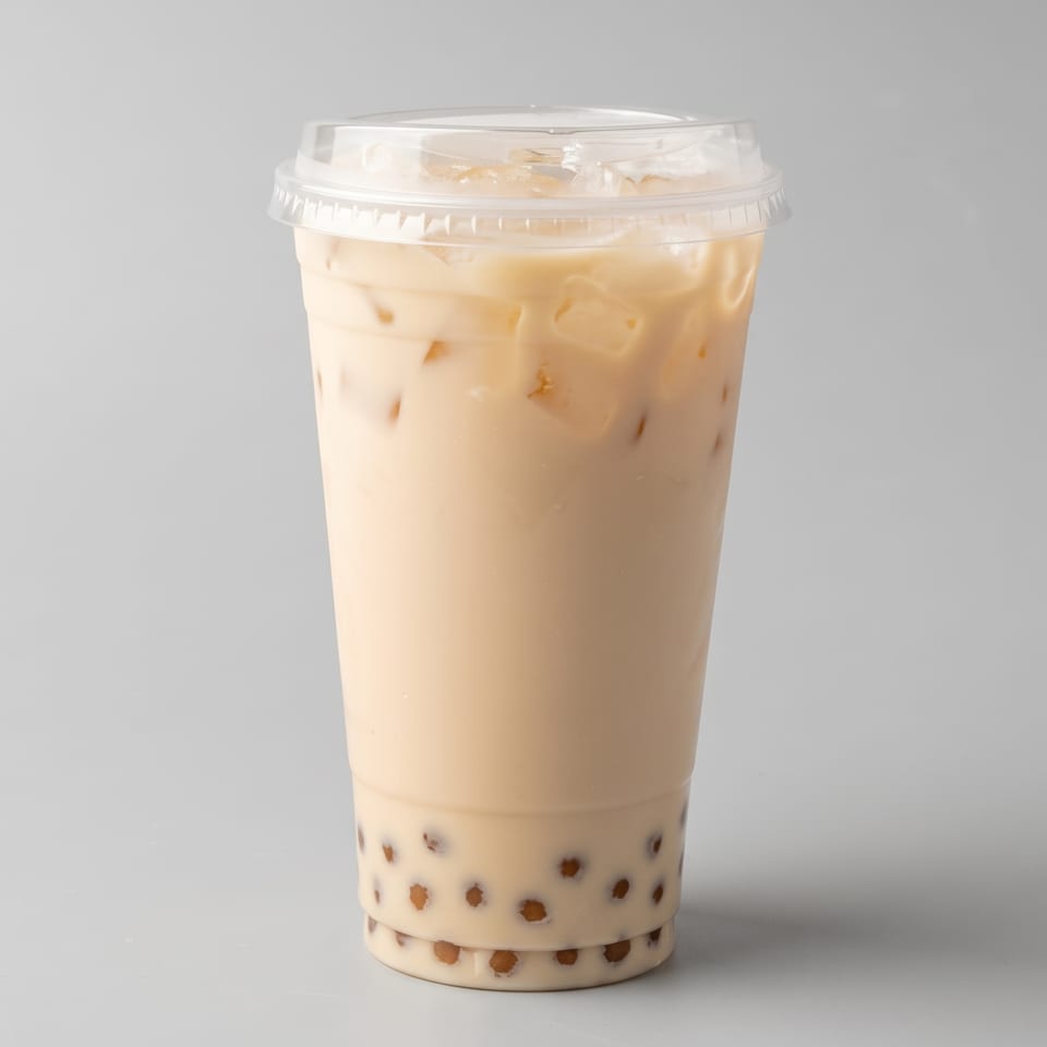 Creamy iced milk tea with tapioca pearls in a clear takeaway cup against a light gray background.